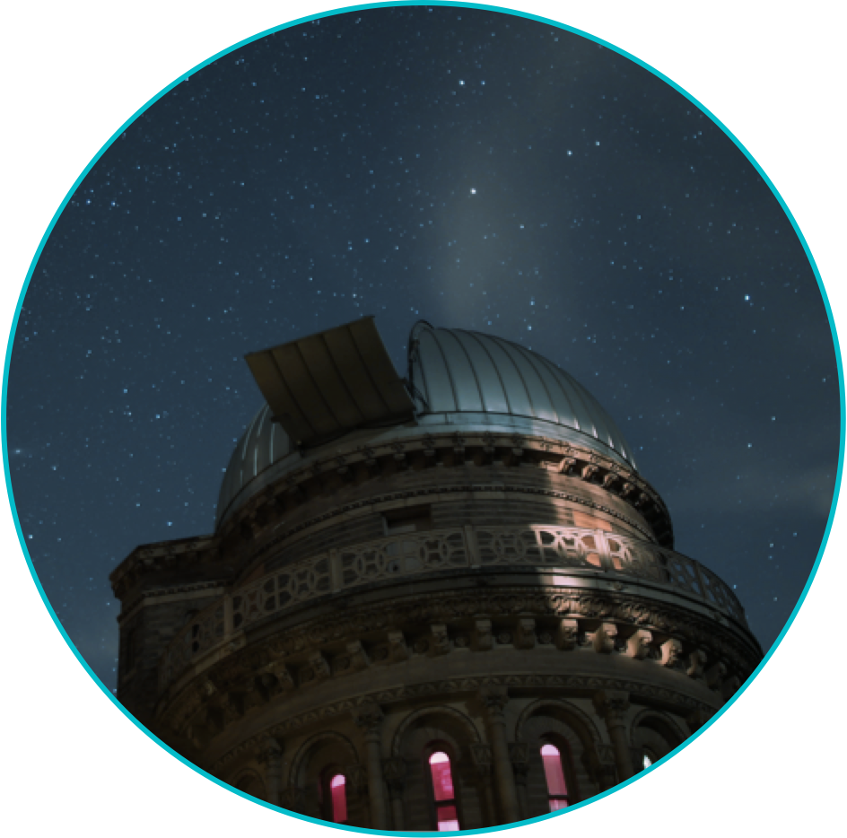 An observatory at night, silhouetted against the starry night sky, consisting of a cylindrical stone structure capped with a metal dome. A hatch on the dome is open, giving a telescope inside a view of the sky.